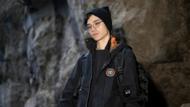 A young adult in a black jacket and beanie inside a rocky cave.