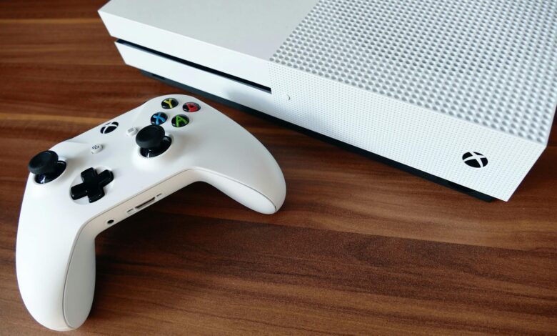 Close-up of a white Xbox console and controller on a wooden surface, ideal for gaming enthusiasts.