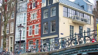 Bicycles lined along a bridge in Amsterdam with historic buildings in the backdrop, showcasing city charm.