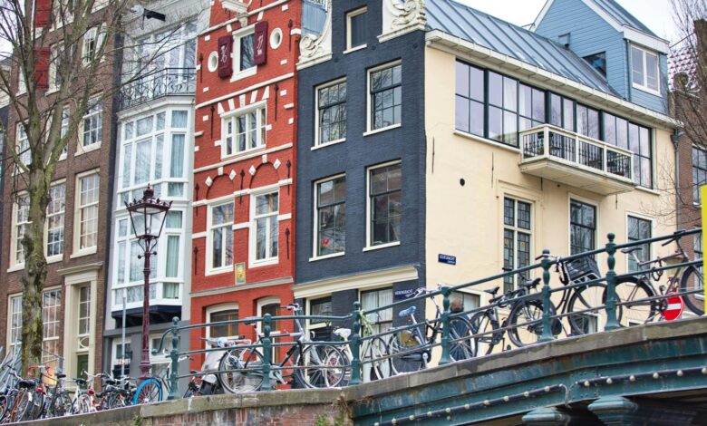 Bicycles lined along a bridge in Amsterdam with historic buildings in the backdrop, showcasing city charm.