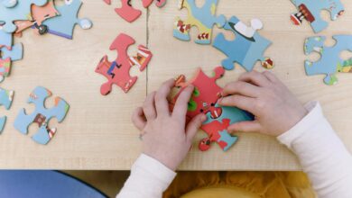 Close-up of child assembling colorful puzzle pieces on a wooden table, top view.