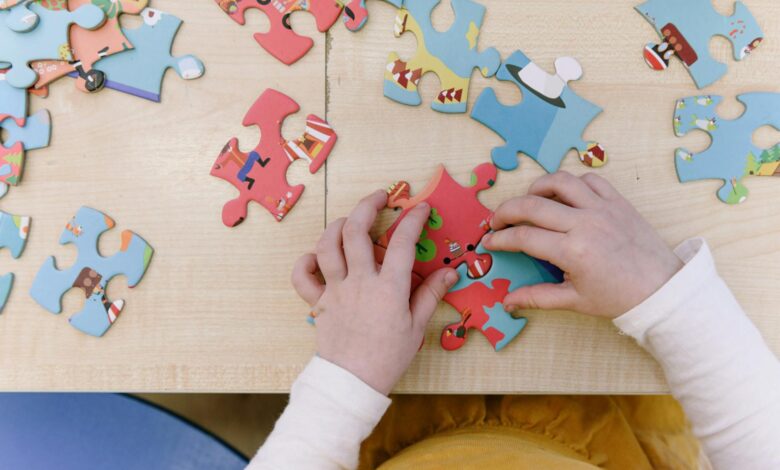Close-up of child assembling colorful puzzle pieces on a wooden table, top view.