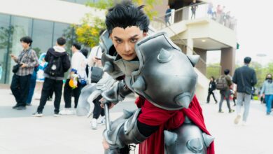 Man in intricate fantasy armor posing at a vibrant outdoor cosplay event.
