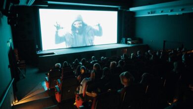 Crowded cinema theater with audience watching a movie on a large screen in a dark setting.