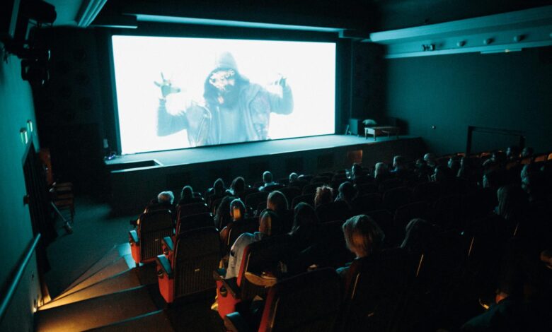 Crowded cinema theater with audience watching a movie on a large screen in a dark setting.