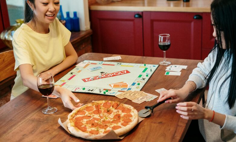 Two friends enjoying a cozy game night with Monopoly and pizza at home.