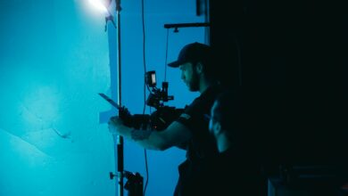 A man adjusts a camera on a film set under moody studio lighting, creating a cinematic atmosphere.