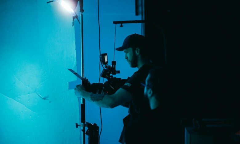 A man adjusts a camera on a film set under moody studio lighting, creating a cinematic atmosphere.