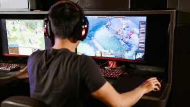 Adult male gamer immersed in PC gaming on dual monitors with headphones indoors.