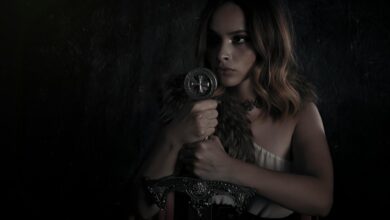 A dramatic and moody portrait of a woman dressed in a medieval warrior costume, holding a sword.