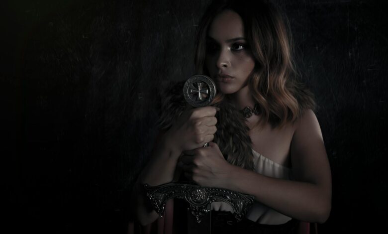 A dramatic and moody portrait of a woman dressed in a medieval warrior costume, holding a sword.