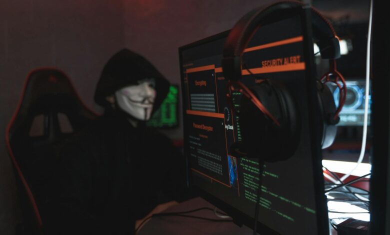 A person wearing a Guy Fawkes mask engaged in hacking activities on a computer in a dimly lit room.