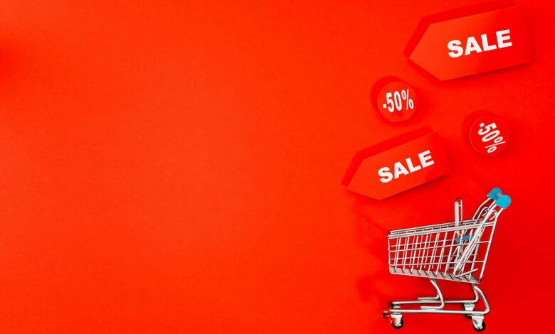 Shopping cart with sale tags on vibrant red backdrop promoting discounts.