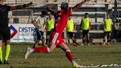 A soccer player in red celebrates a goal with enthusiasm on an outdoor field.
