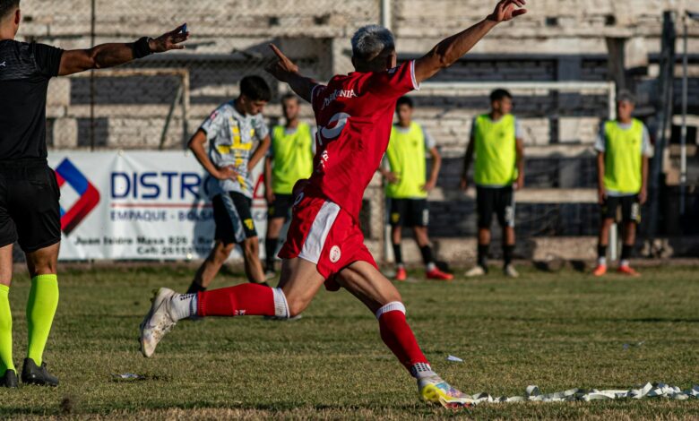 A soccer player in red celebrates a goal with enthusiasm on an outdoor field.