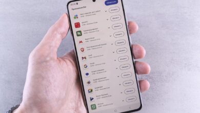 Close-up of a hand holding a smartphone displaying app updates on a light background.