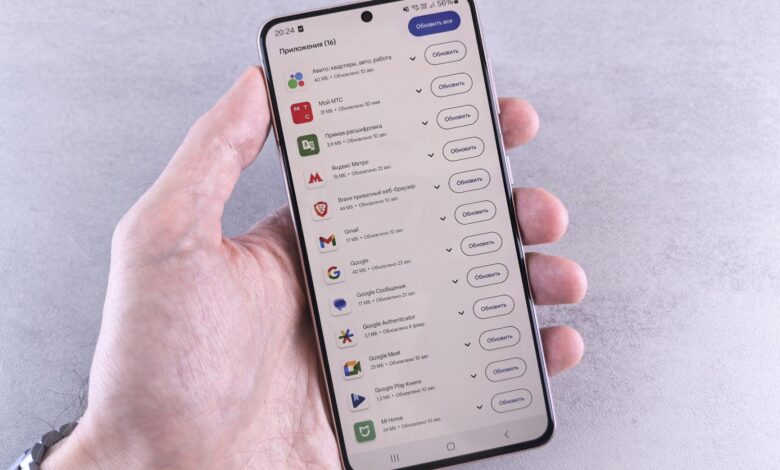 Close-up of a hand holding a smartphone displaying app updates on a light background.