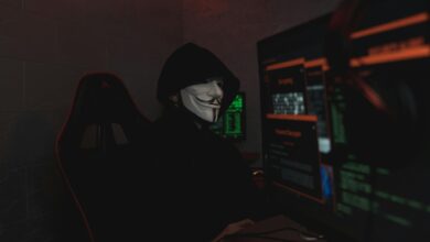 An anonymous hacker wearing a mask working on a computer in a dark room.