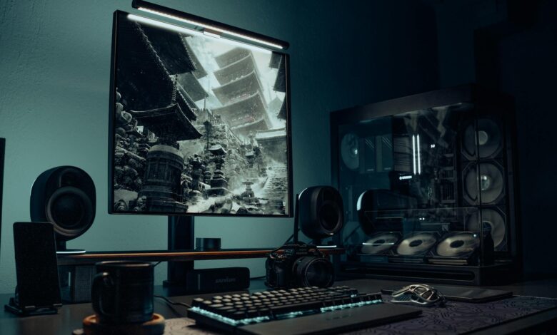 A sleek gaming desk setup with illuminated PC, monitor displaying Asian temple image, and accessories.