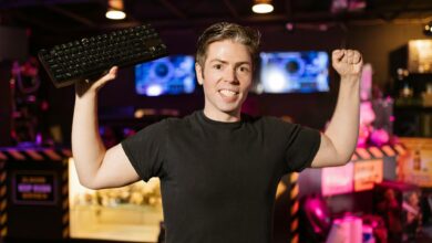 Smiling gamer in black shirt holding keyboard, celebrating indoors with gaming setup.
