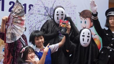 Group of people in cosplay costumes posing at an anime-themed celebration with props and masks.