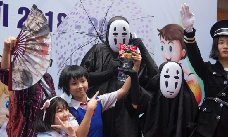 Group of people in cosplay costumes posing at an anime-themed celebration with props and masks.