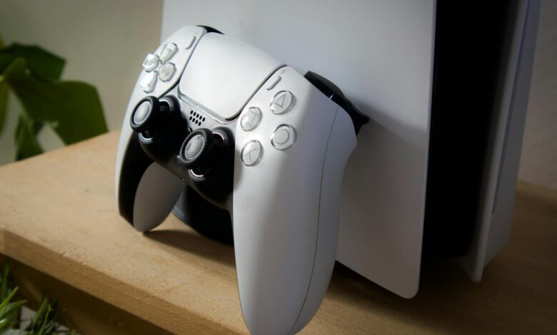 Close-up of PlayStation 5 with DualSense controller on a wooden shelf.