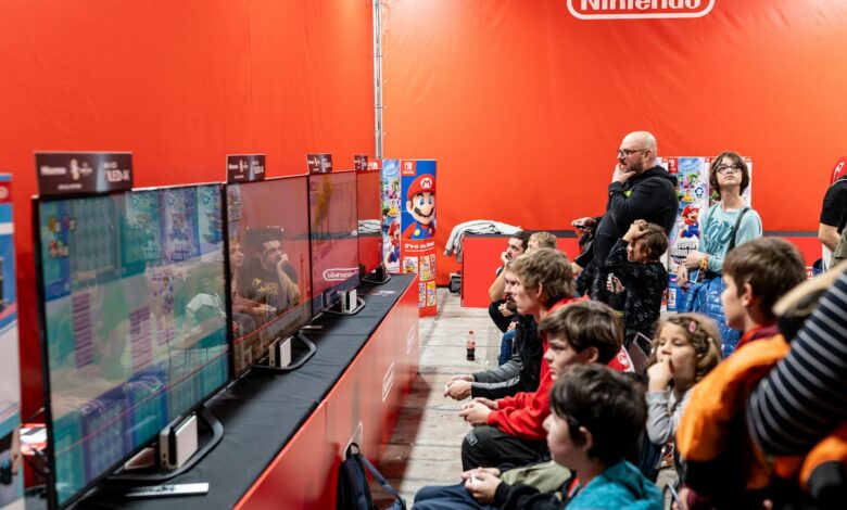 A lively group enjoys gaming at a Nintendo event in Zagreb, featuring multiple screens and vibrant atmosphere.