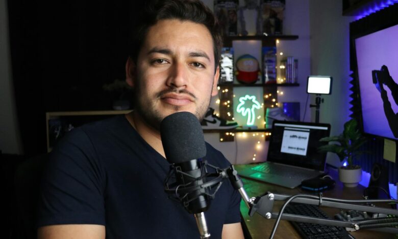 A podcaster in a home studio with neon lighting and tech equipment.