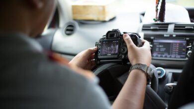 Photographer holding DSLR camera inside car, checking images and settings.
