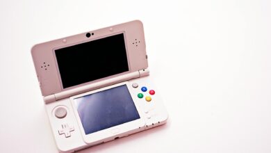 A clean shot of a white portable gaming console with two screens.