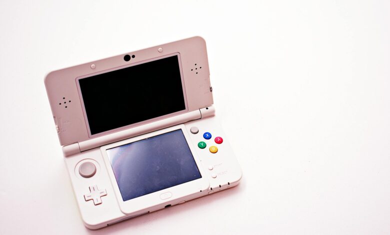 A clean shot of a white portable gaming console with two screens.
