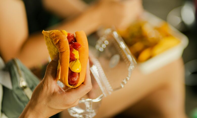 Close-up of a hot dog with mustard and ketchup held in hand, perfect street food meal.