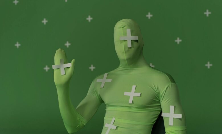 Person wearing a green screen suit with tracking markers for visual effects work.