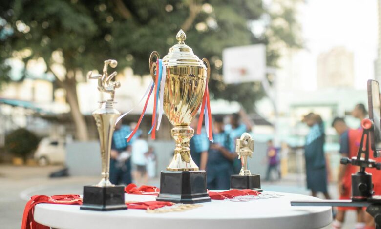 A golden trophy displayed on a table during an outdoor sports event with blurred players in the background.