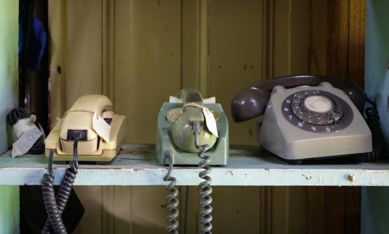 Collection of vintage rotary and push-button telephones on a shelf.