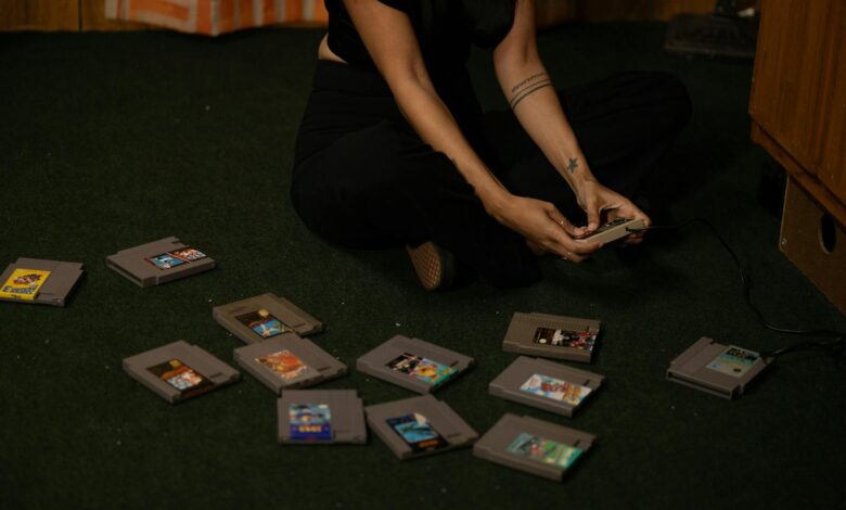 Adult woman sitting cross-legged, holding a vintage game controller, surrounded by retro game cartridges.