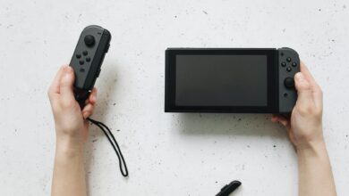 Close-up of hands holding a Nintendo Switch and Joy-Con controllers on a white surface.