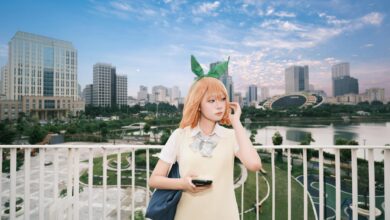 A cosplayer dressed as an anime character poses in a modern city park with a skyline backdrop.