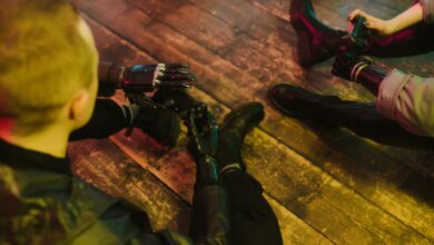 Two people with prosthetic hands playing video games on a wooden floor.