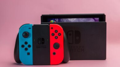 Close-up of Nintendo Switch console with red and blue Joy-Con controllers on pink background.