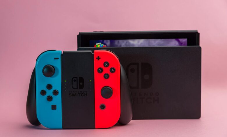 Close-up of Nintendo Switch console with red and blue Joy-Con controllers on pink background.
