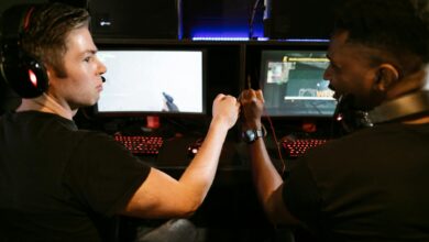 Two male friends fist bump at a computer gaming station, showcasing teamwork and camaraderie.