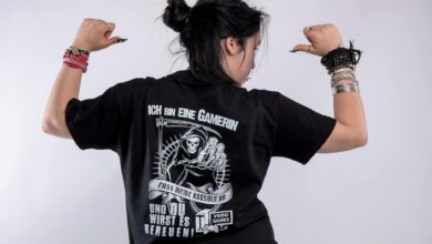 Back view of a woman in black shirt with gaming graphics, posing confidently in a studio.