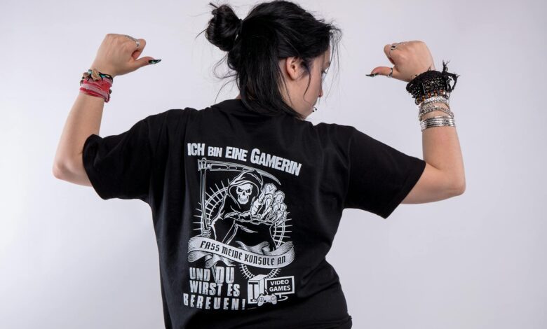 Back view of a woman in black shirt with gaming graphics, posing confidently in a studio.