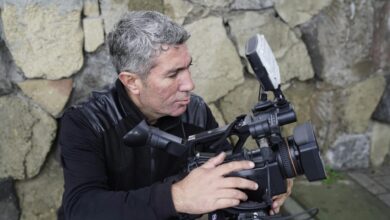 Experienced filmmaker adjusting a professional video camera outdoors.