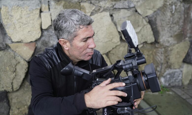 Experienced filmmaker adjusting a professional video camera outdoors.