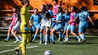 A women's soccer team celebrating after scoring a goal during a daytime match.