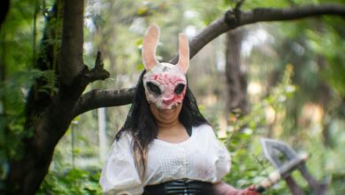 Cosplayer in a forest wearing a distinctive mask, conveying a mysterious theme.