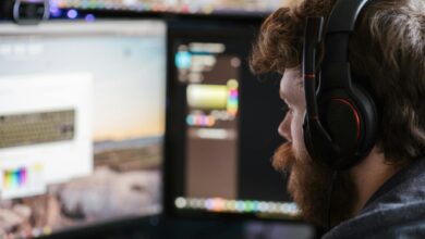 Side view concentrated bearded male in headphones using modern computer and looking at multiple monitors
